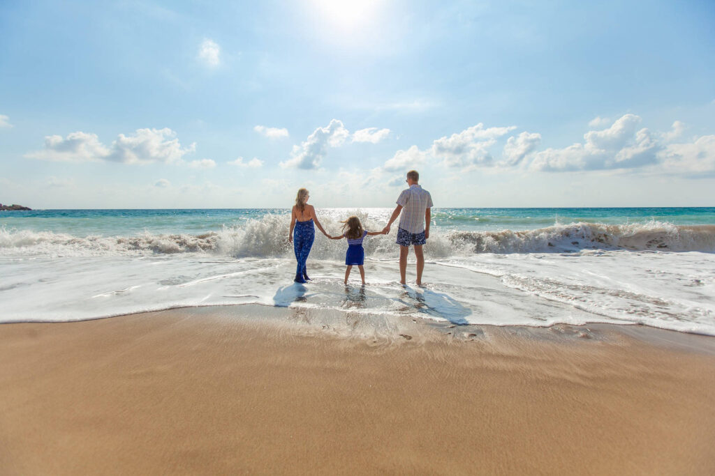 Drei Personen stehen am Sandstrand der Seychellen und blicken auf das blaue Meer mit Wellen und klarem Himmel