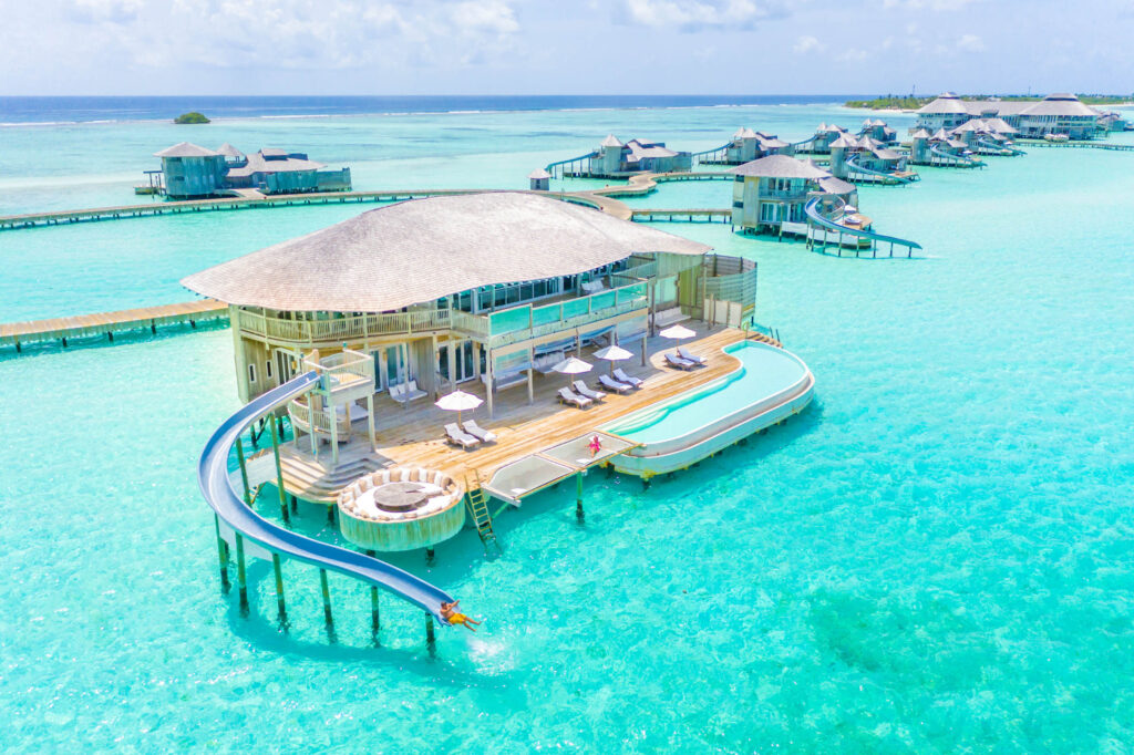 Überwasser-Bungalow auf Pfählen mit Holzbau, Schilfdach, Infinity-Pool und Rutsche ins türkisfarbene Meer