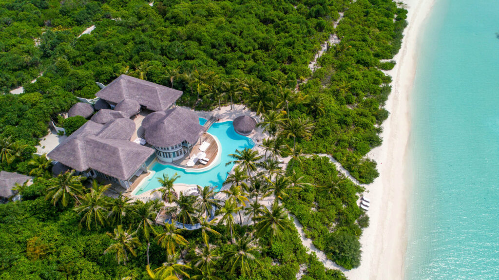 Vogelperspektive auf Resort Soneva Jani mit strohgedeckten Dächern, Pool, Palmen und weißem Sandstrand