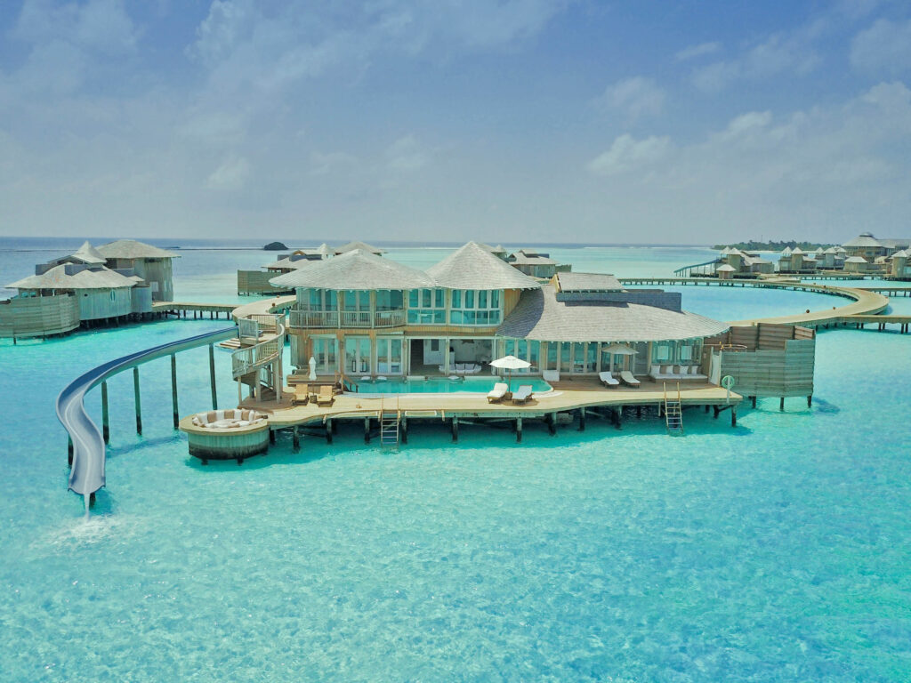 Resort auf Stelzen mit hellen Holzwänden und großer Wasserrutsche ins türkisfarbene Meer