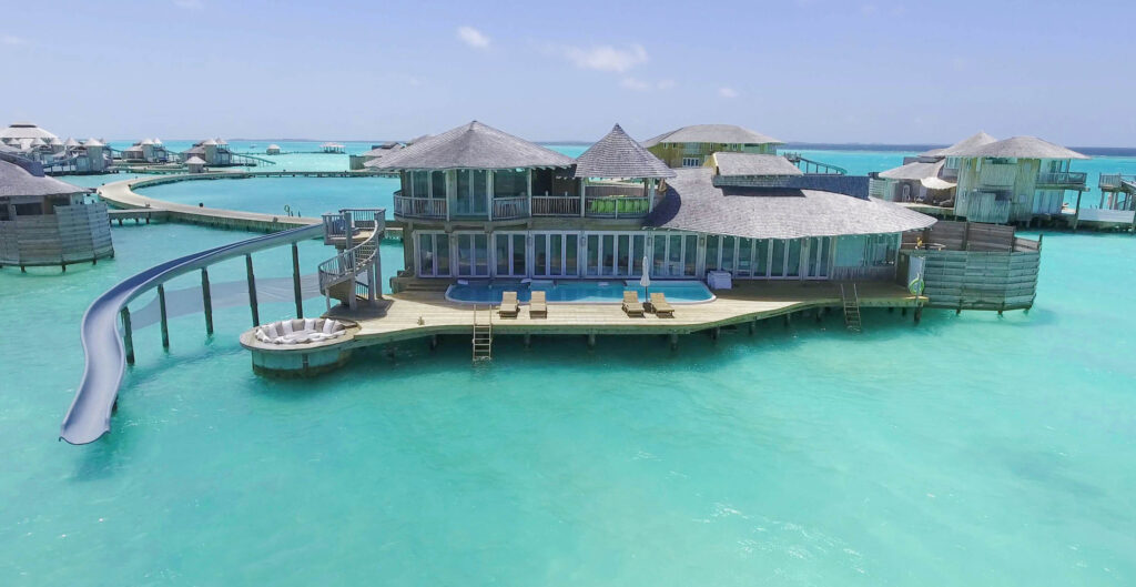 Resort-Haus auf Stelzen mit Holzdeck, Pool und Wasserrutsche über türkisfarbenem Meer
