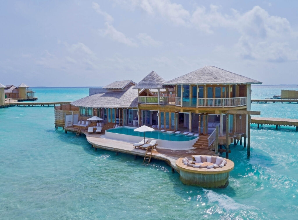 Wasser-Villa auf Stelzen mit Holzarchitektur, Terrasse, Pool und Lounge-Bereich über türkisblauem Meer