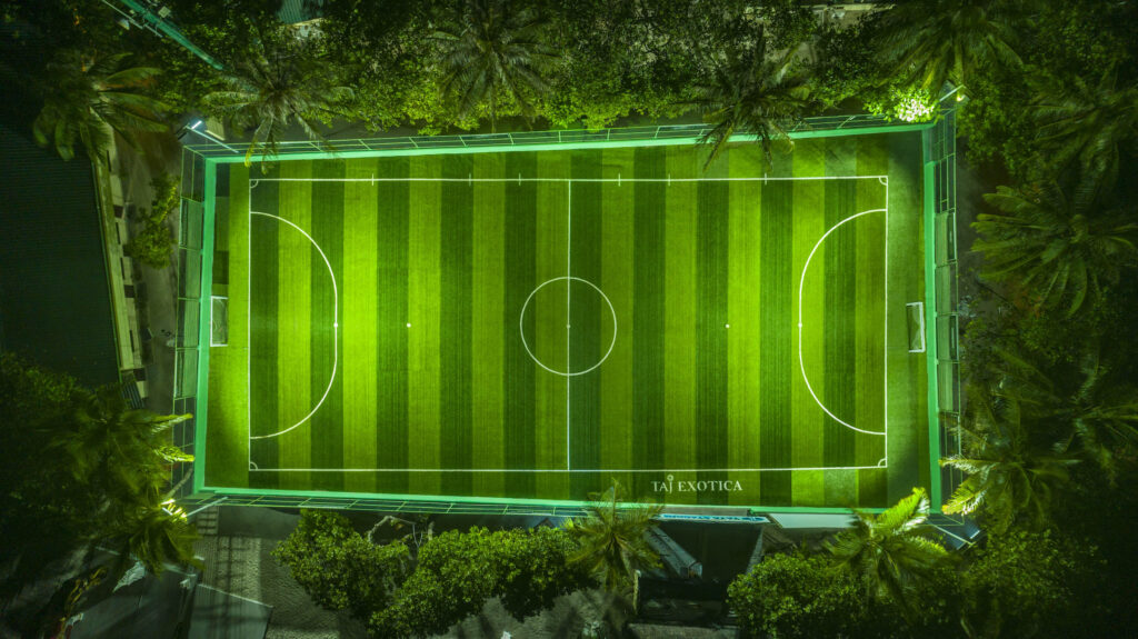 Vogelperspektive eines Fußballplatzes mit gestreiftem grünen Rasen und weißen Linien, umgeben von Palmen bei künstlicher.