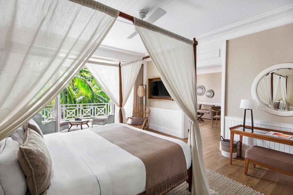 Hell eingerichtetes Hotelzimmer mit Himmelbett, Holzfußboden und Balkon mit Blick auf grüne Palmen in Mauritius