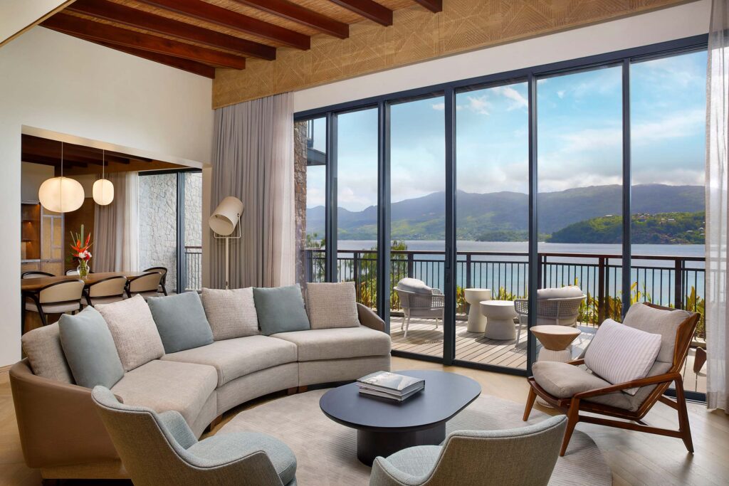 Wohnzimmer mit grauer Couch, Holzfußboden und großen Fenstern mit Blick auf See