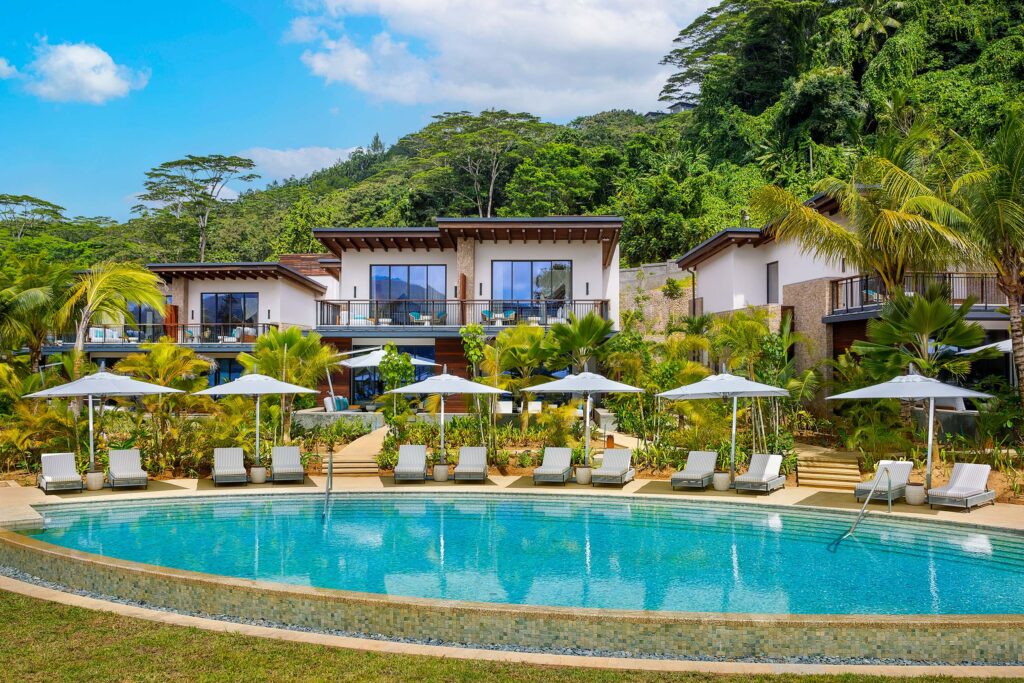 Hotel Mango House mit großem geschwungenem Pool, gepolsterten Sonnenliegen und weißen Sonnenschirmen vor moderner Architektur
