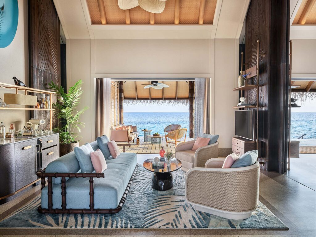 Hotelzimmer mit hellblauem Sofa, beigen Sesseln, Holzdecke und offener Terrasse zum Meer auf den