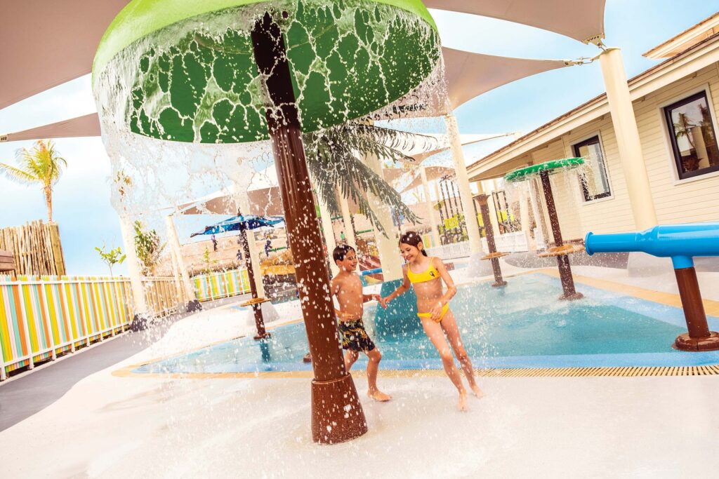 Wasserparkbereich mit spielenden Kindern unter grüner Wasserkuppel und rutschfestem Boden