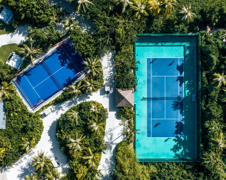 Zwei Tennisplätze mit türkis-blauer und dunkelblauer Oberfläche umgeben von Palmen auf den