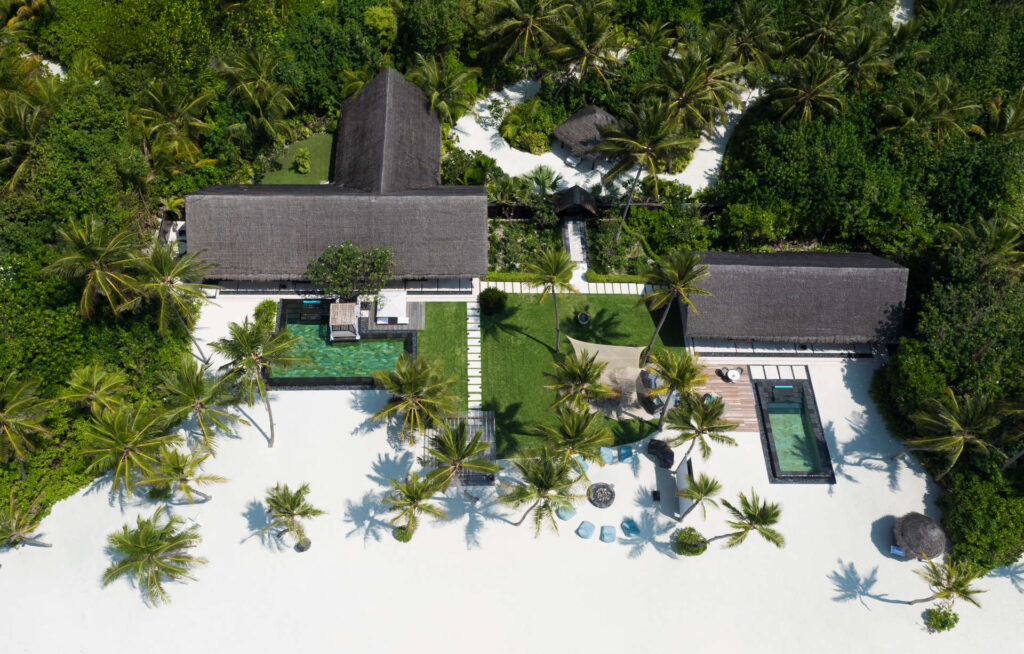 Tropisches Resort One&Only Reethi Rah mit strohgedeckten Bungalows, zentralem Pool, Palmen und Sandflächen.