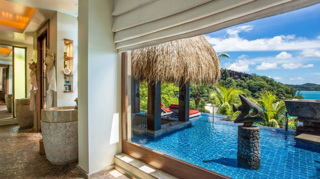 Badezimmer mit poliertem Steinwaschbecken, quadratischen Erdtönen Fliesen und Infinity-Pool mit Fischskulptur im Hintergrund