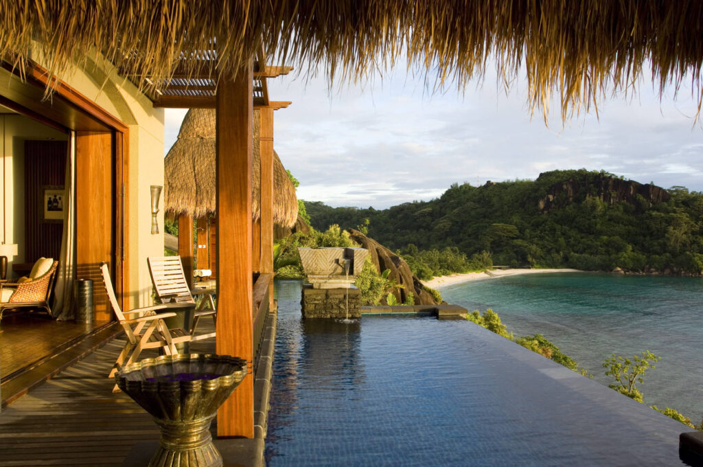 Terrasse mit Holz und Stein, Infinity-Pool, Meer im Hintergrund, natürliche Beleuchtung am Morgen oder Abend