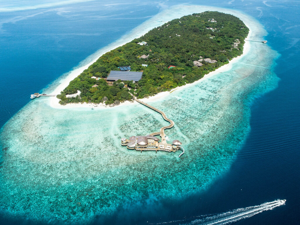 Luftaufnahme einer tropischen Insel mit grüner Vegetation, Steg und über Wasser gebauten Holz-Glas-Bungalows auf den.
