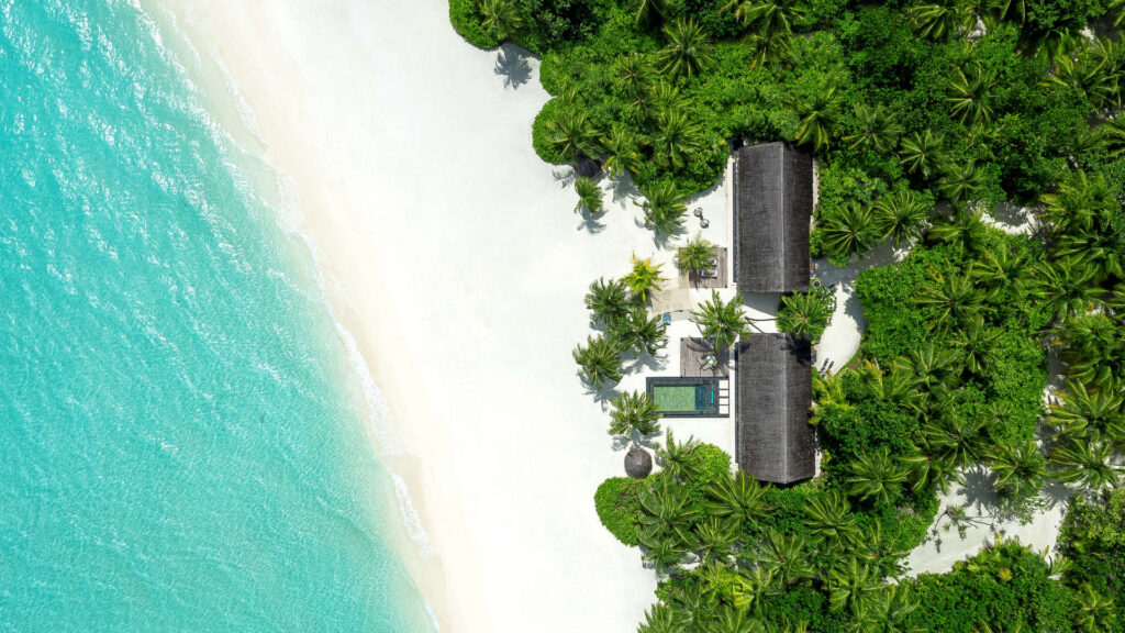 Luftaufnahme des One&Only Reethi Rah Resorts mit weißem Sandstrand, türkisfarbenem Meer, zwei Gebäuden und Pool auf den.