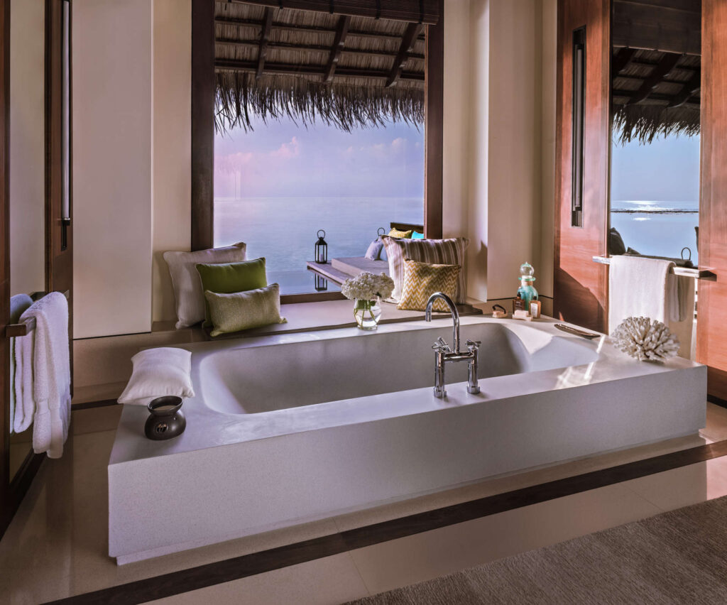 Badezimmer mit freistehender weißer Badewanne, großen Fenstern mit Blick auf das offene Meer und natürlichem Holzdecke