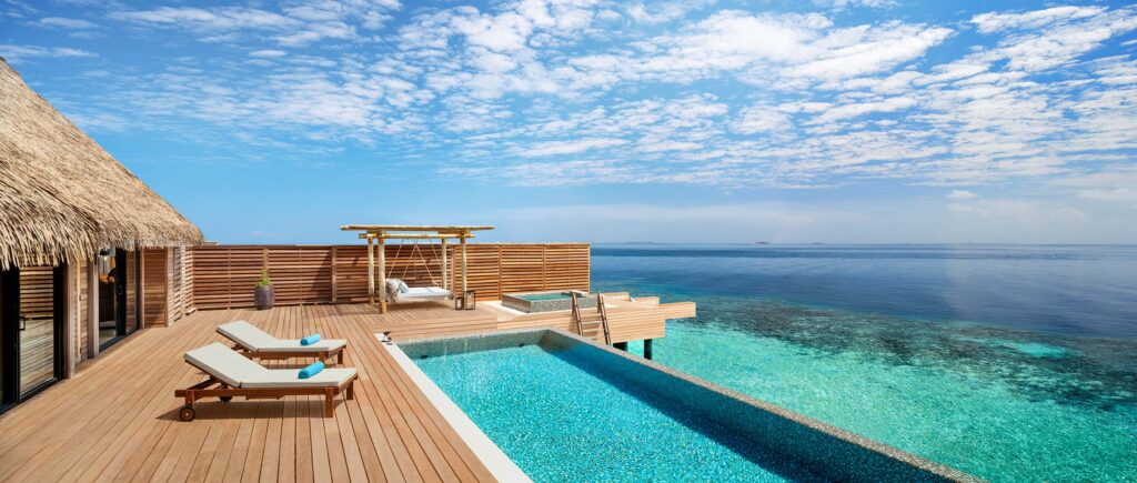 Terrasse über dem Meer mit Holzdeck, Pool, zwei Liegestühlen mit blauen Handtüchern und Pavillon mit Schilfdach