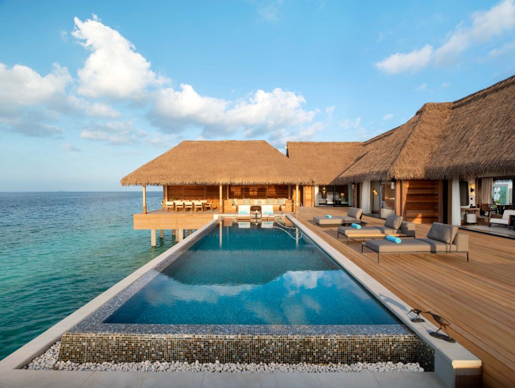 Wasservillen auf Stelzen mit Holzterrassen und Strohdach über dem Meer, Infinity-Pool im Vordergrund