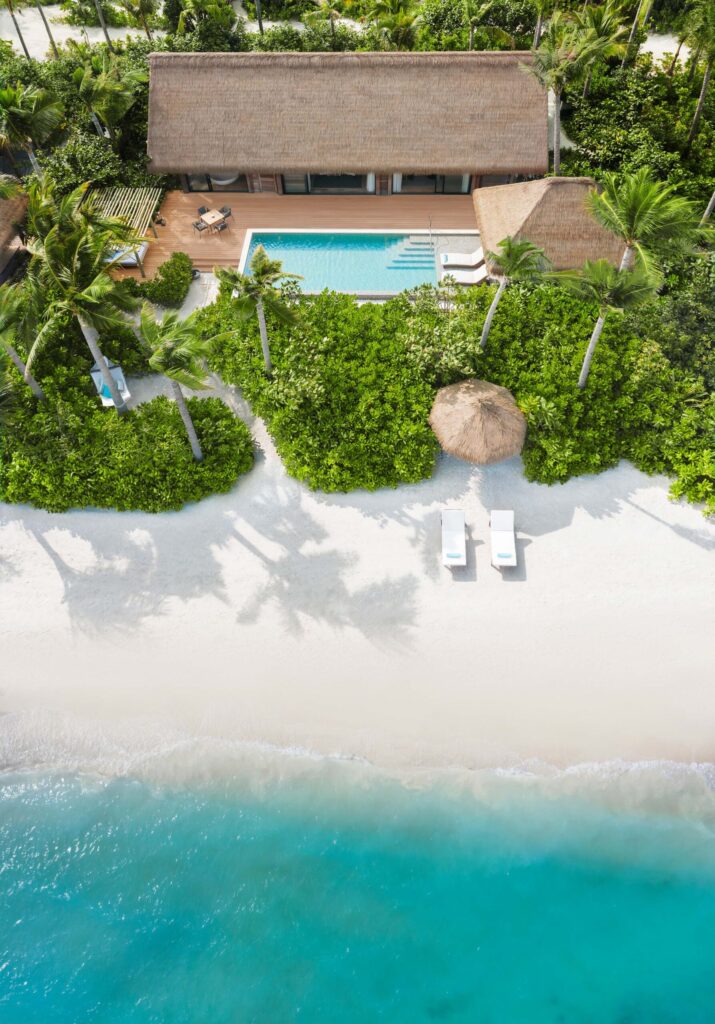 Vogelperspektive auf rechteckigen Pool mit Holzterrasse und Strohdachgebäude an tropischem Strand auf den