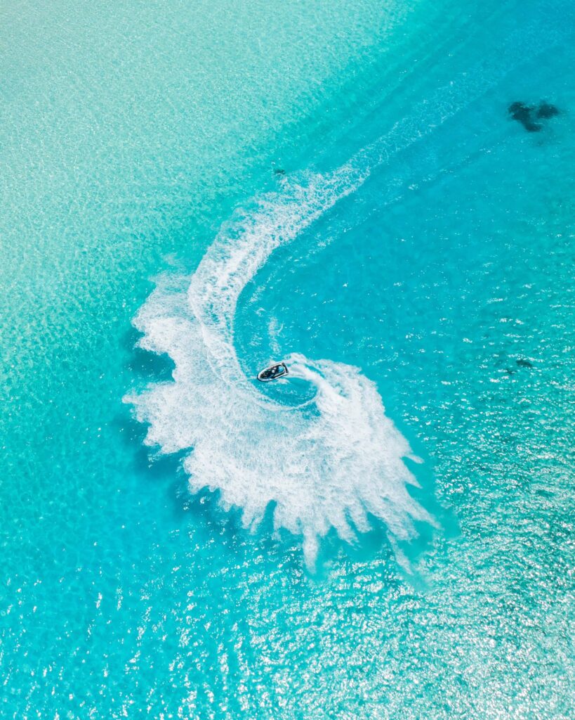Drohnenaufnahme eines Jetskis auf türkisblauem Meer mit weißer Schaumspur und Wellenmustern