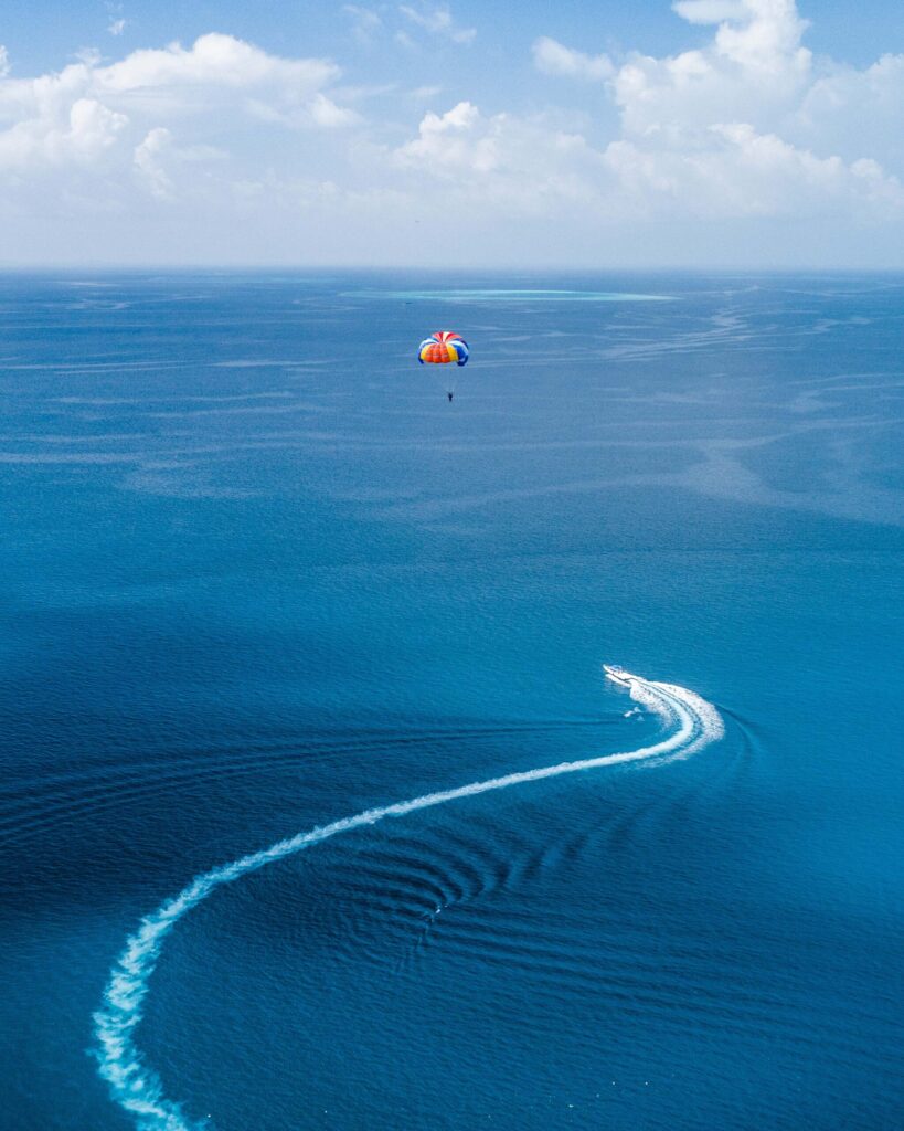 Person beim Parasailing hinter Motorboot auf offenem Meer mit blauem Himmel und türkisfarbenem Wasser
