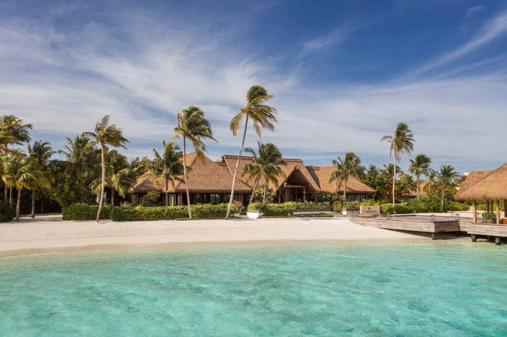 Resort am Strand mit strohgedeckten Holzdächern, Palmen und türkisfarbenem Wasser auf den