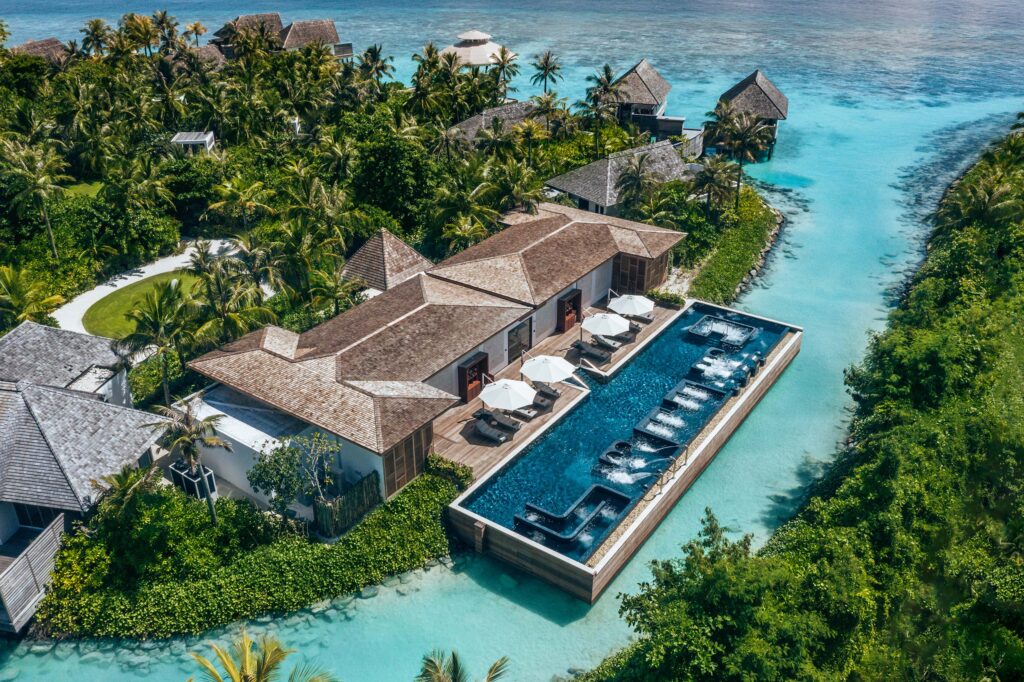 Waldorf Astoria Maldives Ithaafushi langgestreckter Pool Resort mit langem Pool entlang eines türkisfarbenen Kanals, Holzdecks mit weißen Sonnenschirmen und Liegen, umgeben von.