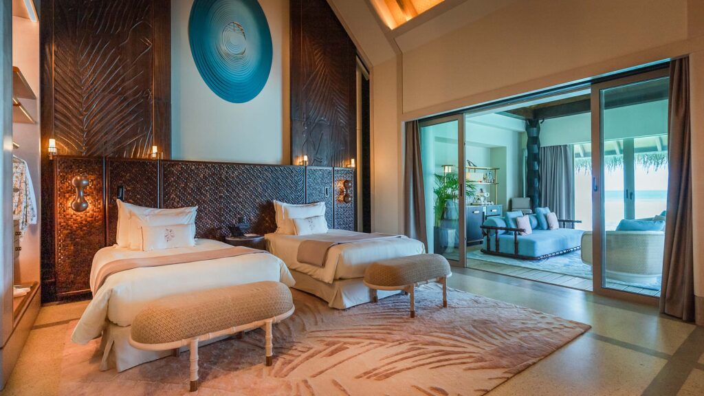 Hotelzimmer mit zwei Einzelbetten, blauen Sesseln und Sofa, Holzvertäfelung und großer Glasschiebetür