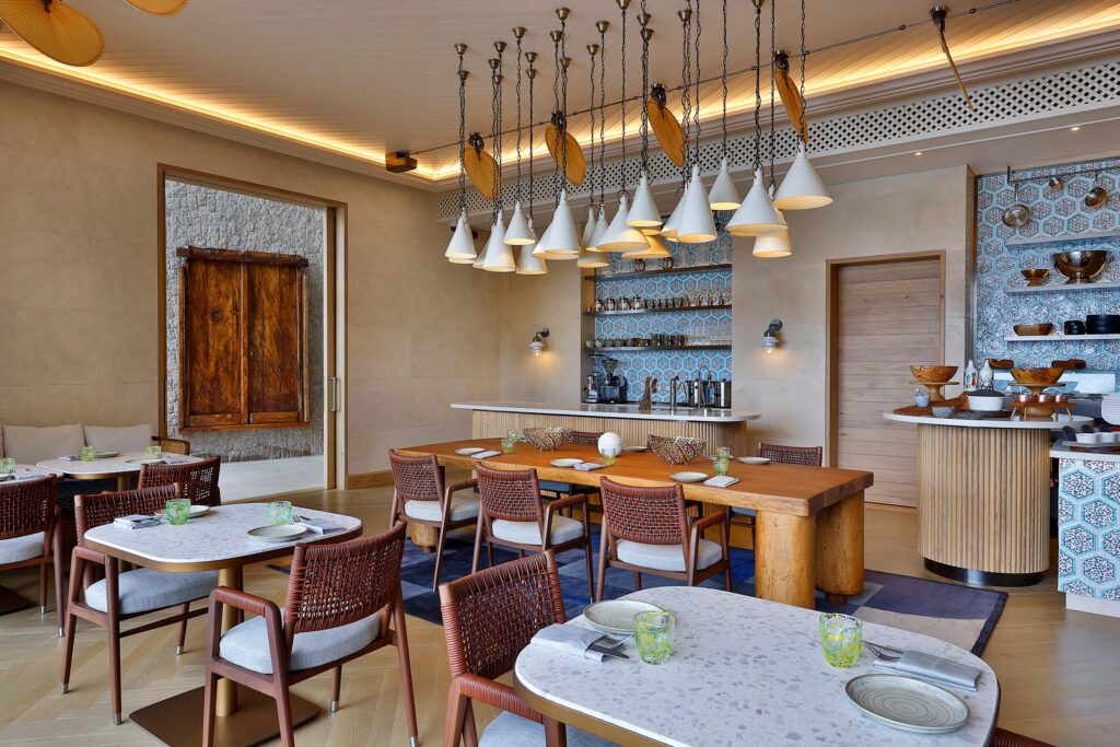 Innenraum eines Hotelrestaurants mit Holztisch, Korbstühlen, blau-weißen Fliesen und moderner Beleuchtung