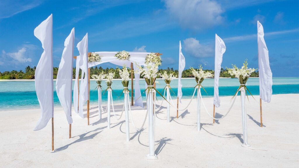 Strandhochzeitskulisse mit weiß dekoriertem Holzpavillon, Blumenständern und türkisblauem Meer im Hintergrund auf den.