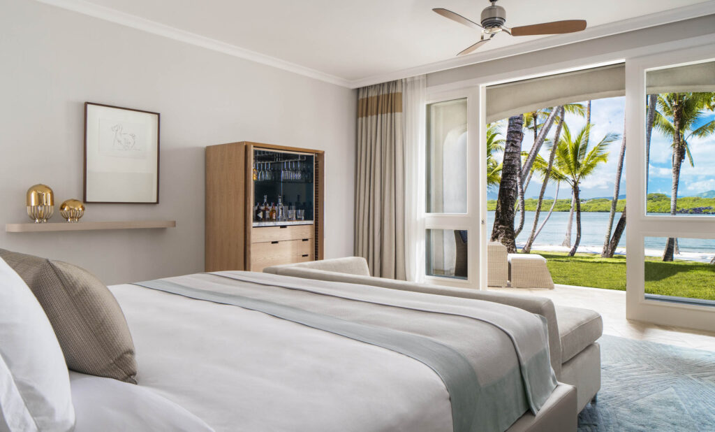 Modernes Hotelzimmer mit großem Bett, weißen und grauen Bettwäschefarben und tropischer Aussicht