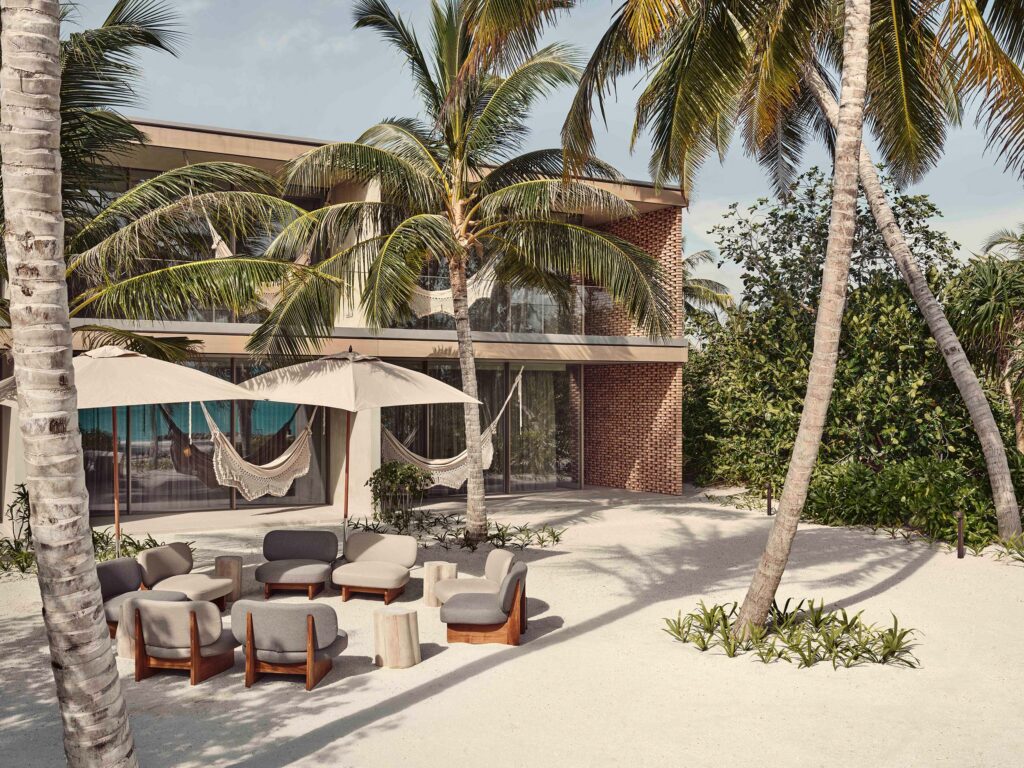 Außenbereich des Patina Maldives Hotels mit Backsteinfassade, grauen Polstersesseln und Hängematten unter Palmen