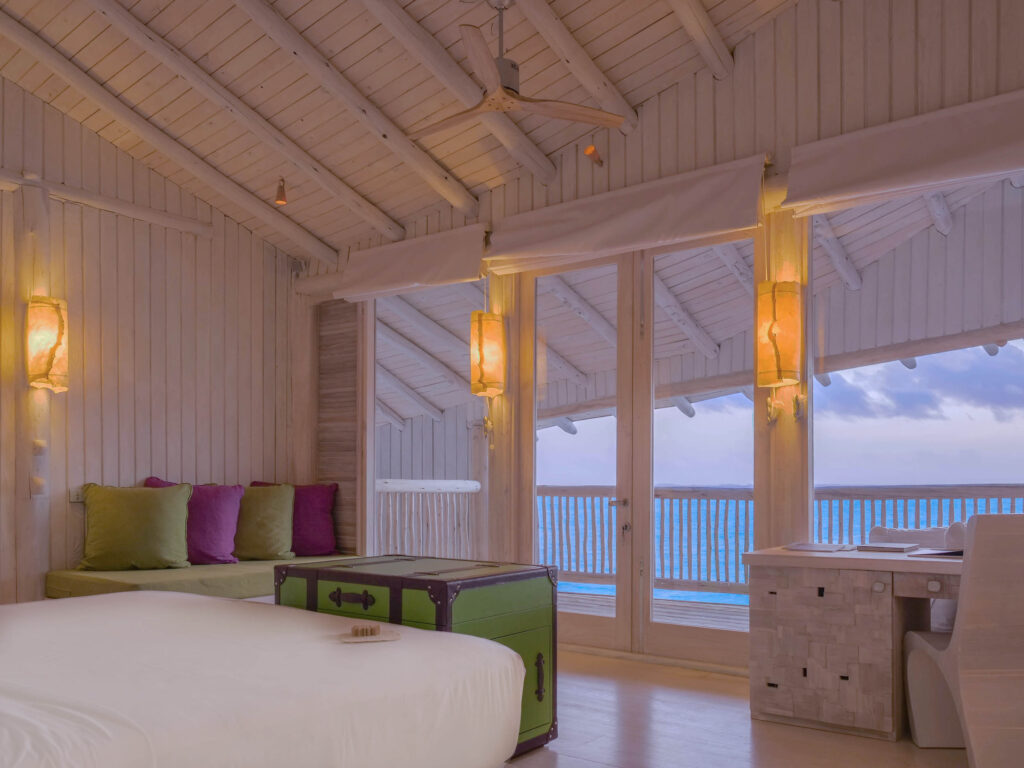 Hotelzimmer in Soneva Jani mit Holzdecken, Sandtönen, großen Fenstern und Blick auf das Meer