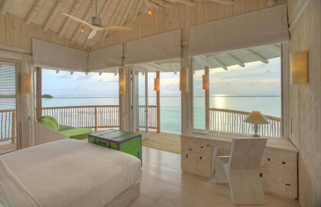 Hotelzimmer mit großen Glasfenstern, hellem Holzmobiliar und Blick auf das Meer bei Tageslicht