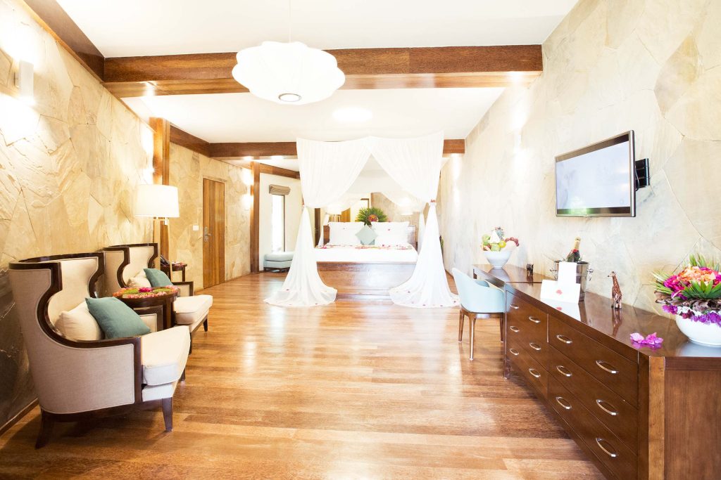Geräumige Hotelsuite mit Himmelbett, weißen Vorhängen, Natursteinwänden und poliertem Holzboden