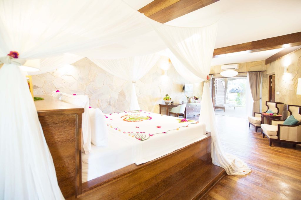 Hotelzimmer mit Himmelbett, weißen Vorhängen, Natursteinwänden, Holzboden und großer Fensterfront zur Terrasse