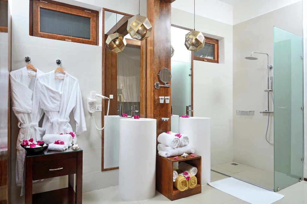 Modernes Badezimmer mit zwei weißen Waschbecken, Holzeinrahmungen, Glasdusche und natürlichem Licht in einem