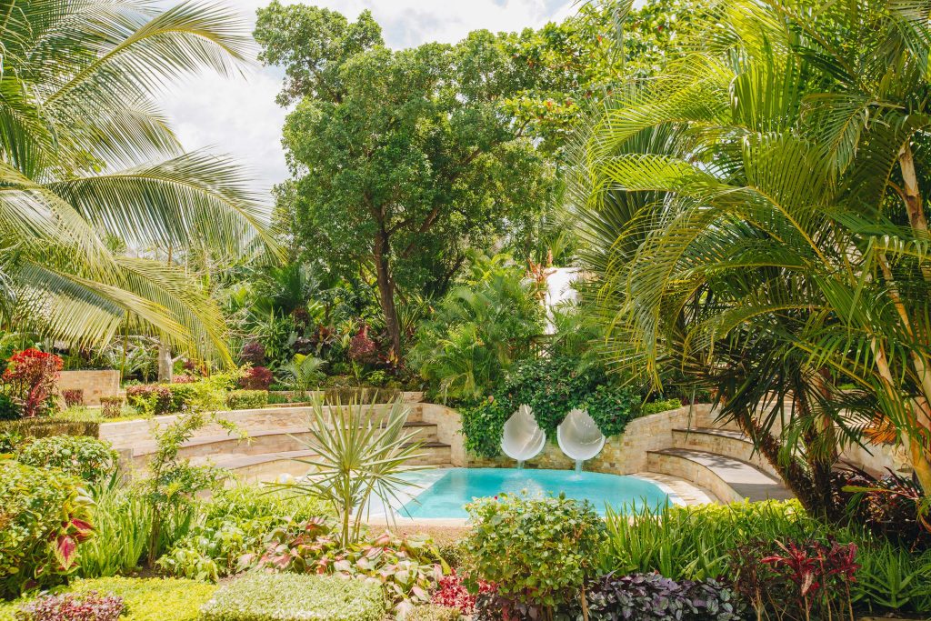 Kleiner Pool mit zwei weißen Rutschen, umgeben von tropischen Palmen und gemauerter Steinwand in Tulia Zanzibar