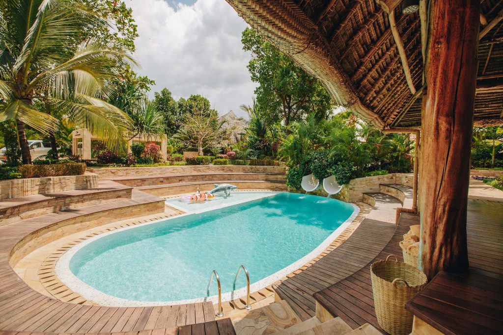 Nierenförmiger Pool mit Holzterrasse, Palmstrohdach und geflochtenem Korb im Tulia Zanzibar Resort