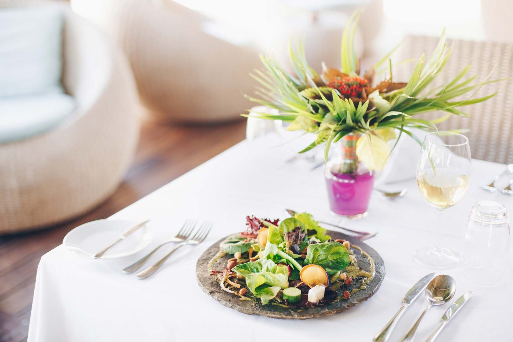 Restauranttisch mit weißem Tuch, Besteck, Weinglas, Wasserglas, Salat und Vase