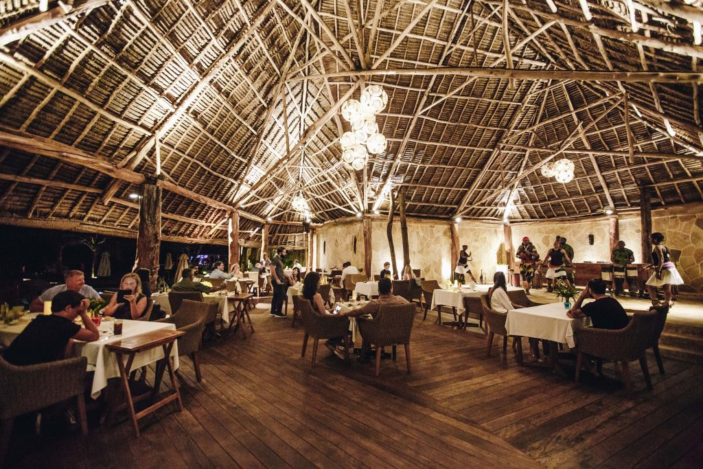 Offenes Restaurant mit hohem Holz-Strohdach, Holzpfosten, Holzboden und Rattanmöbeln im Tulia Zanzibar Hotel