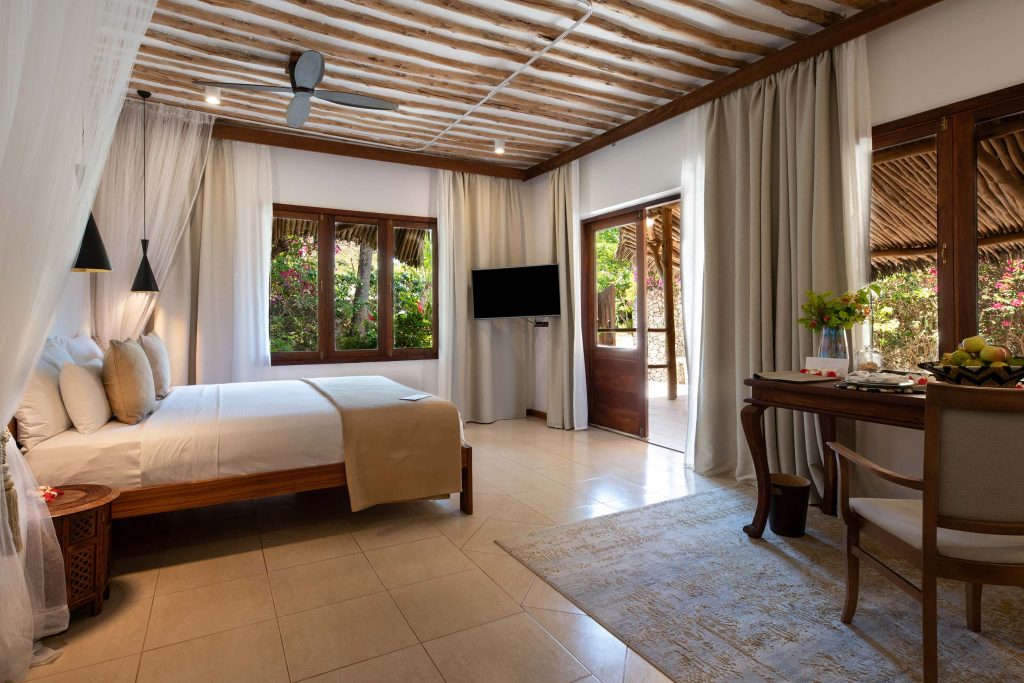 Hotelzimmer mit weißem Baldachinbett, Holzelementen, Schreibtisch und großen Fenstern mit Blick ins Freie