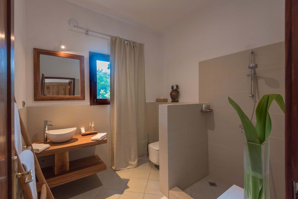 Badezimmer mit Waschbecken auf hölzerner Konsole, großem Spiegel, Fenster mit grünem Baum draußen und Dusche mit Vorhang