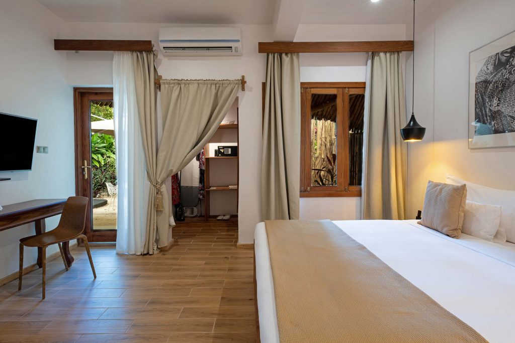 Modernes Hotelzimmer mit großem Bett, Holzmöbeln, Flatscreen-TV und Blick auf begrünte Außenanlage