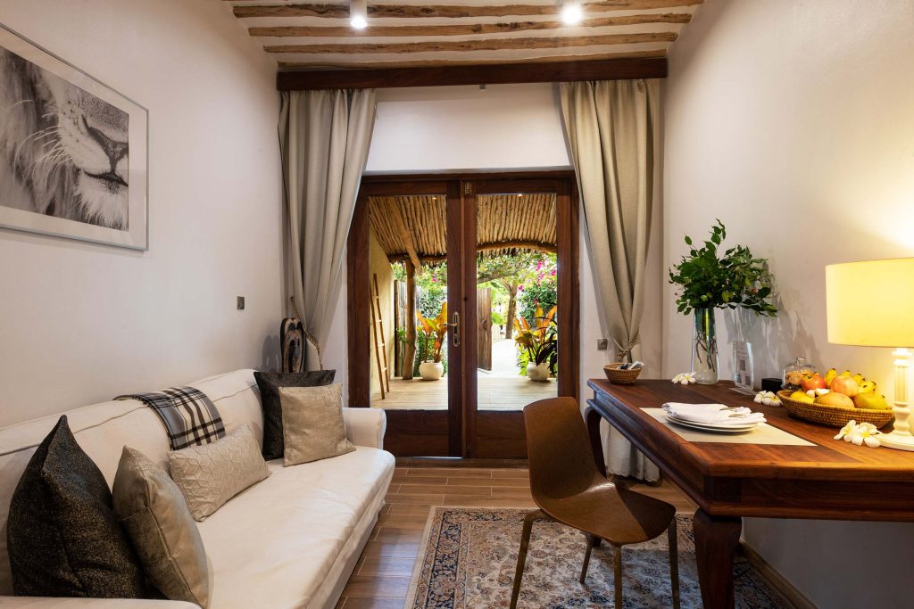 Hotelzimmer mit Holzschreibtisch, braunem Stuhl, hellen Sofa und Terrasse mit Pflanzen in Sansibar