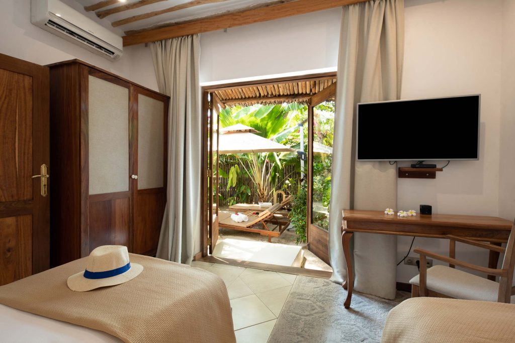 Hotelzimmer mit Holzmöbeln, Schreibtisch, Flachbildfernseher und Terrasse mit Liegestühlen in Sansibar