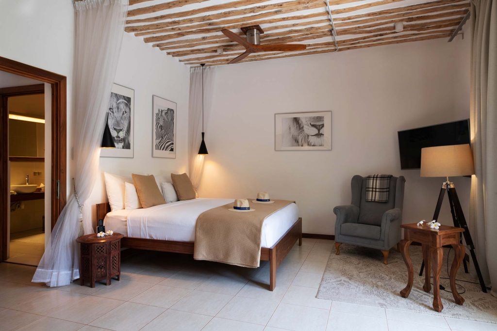 Hotelzimmer mit Doppelbett, Holzmöbeln, grauem Sessel und schwarz-weißen Tierbildern über dem Bett