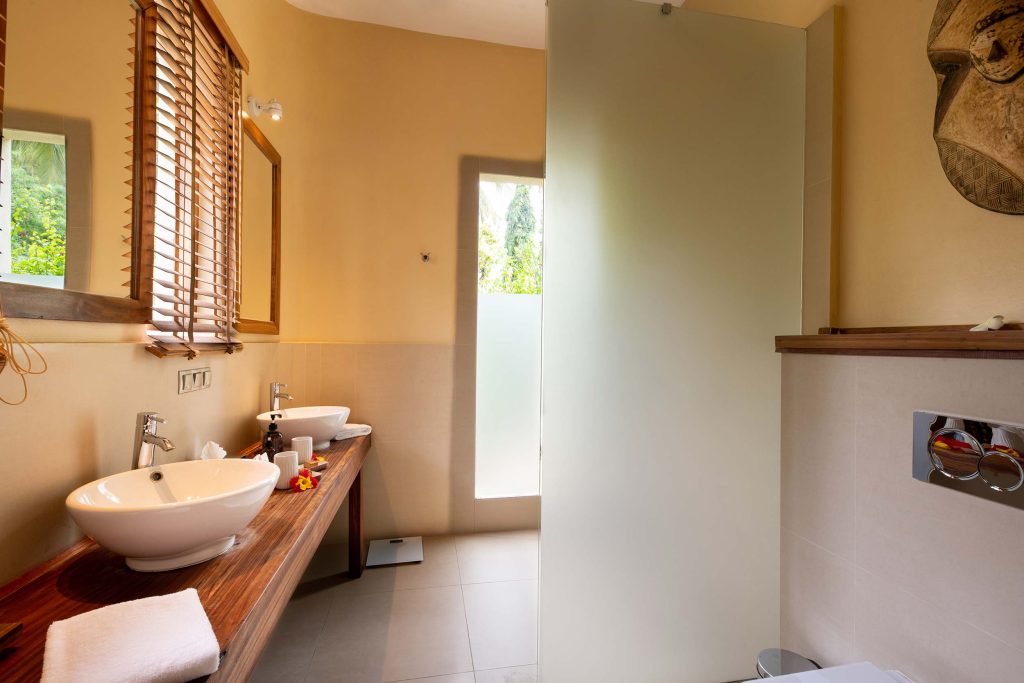 Badezimmer mit zwei ovalen Waschbecken auf Holzarbeitsplatte, Fenster mit Lamellenjalousien, rechteckige Toilette