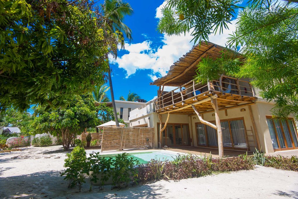 Zweistöckiges Hotelgebäude mit hellen Holzbalken und kleinem Pool in tropischer Vegetation in Sansibar