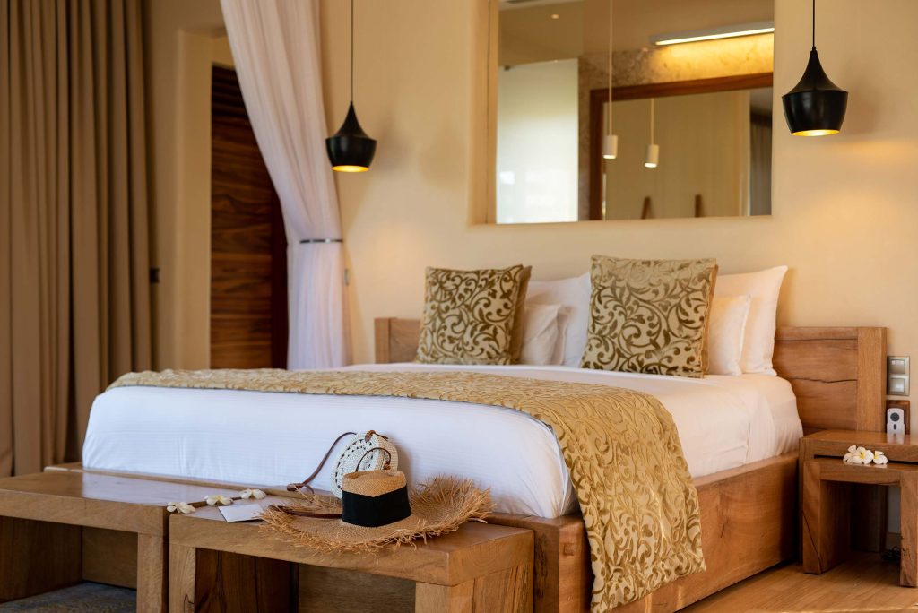 Hotelzimmer mit großem Bett, hölzerner Rahmenkonstruktion, gold gemusterten Kissen und warmem Licht in Sansibar