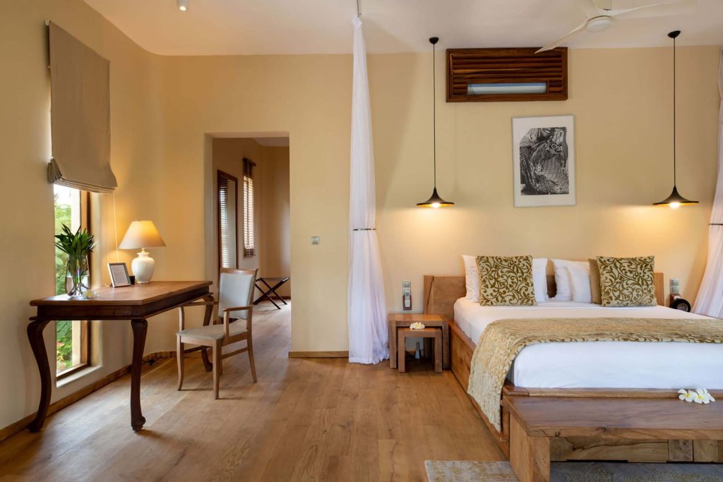 Hotelzimmer mit großem Bett, Holzschreibtisch, Stuhlgruppe, Steinboden und natürlichem Licht in Sansibar